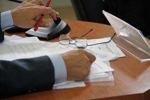 #PraCegoVer: Foto mostra as mãos de um vereador sobre a mesa e sobre documentos. Também há um óculos na bancada.