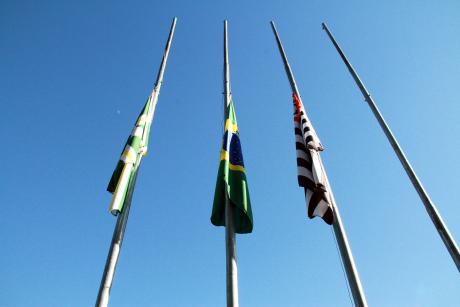 #PraCegoVer: Bandeiras de Valinhos, do Brasil e do estado de São Paulo estão hasteadas na metade do mastro, em sinal de luto. Ao fundo, o céu sem nuvens.