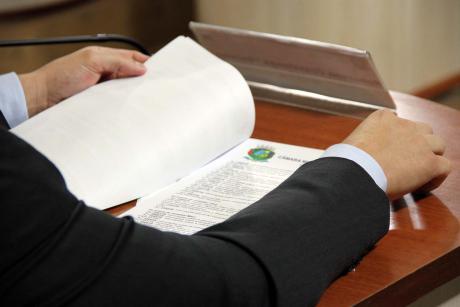 #PraCegoVer: Foto mostra o braço de um vereador sobre a mesa, folheando um documento
