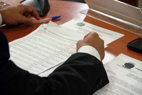 #PraCegoVer: Foto mostra os braços de um vereador apoiados na mesa, folheando um documento.