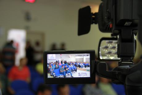 #PraCegoVer: Foto mostra detalhe da câmera filmadora da TV Câmara, resgistrando imagem do público que acompanha a sessão.