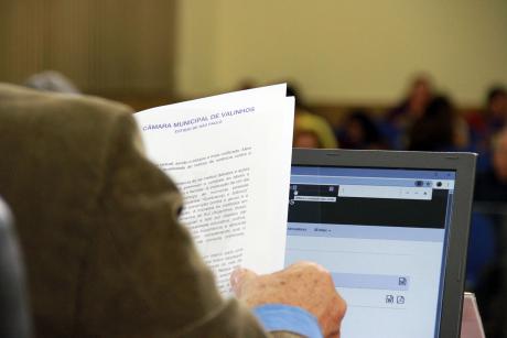 #PraCegoVer: Foto mostra vereador de costas, lendo um documento durante a sessão ordinária