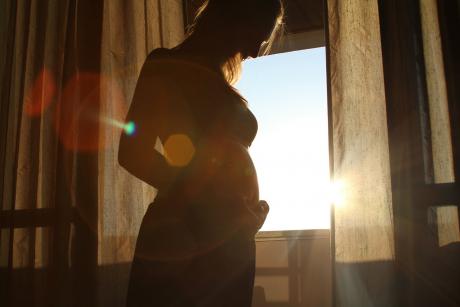 #PraCegoVer: Foto mostra silhueta de jovem grávida olhando para a barriga, com sol se pondo