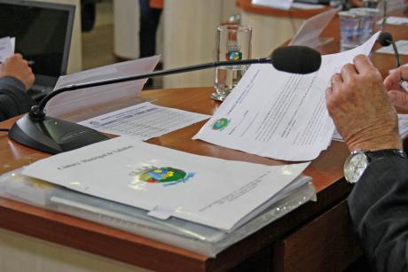 #PraCegoVer: Foto mostra a mão de um vereador sobre a mesa, folheando documentos durante a sessão ordinária.