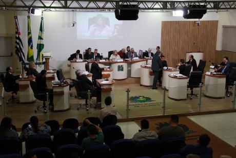 #PraCegoVer: Foto mostra o plenário da Câmara visto de cima, com os vereadores sentados em seu lugares e parte do público assistindo à sessão. 
