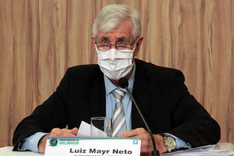 #PraCegoVer: Mayr segura um papel e olha para a frente de sua tribuna à mesa diretora da Câmara. Ele veste uma máscara branca.