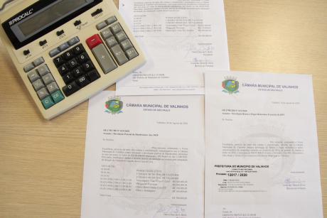 #PraCegoVer: Foto mostra calculadora financeira e três documentos que comprovam a devolução de recursos feita pela Câmara Municipal. 