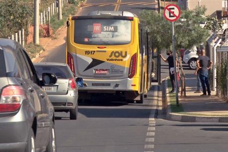 #PraCegoVer: Homem segura porta de ônibus da Sou Valinhos e conversa com alguém no interior do veículo em rua com ponto de ônibus descoberto