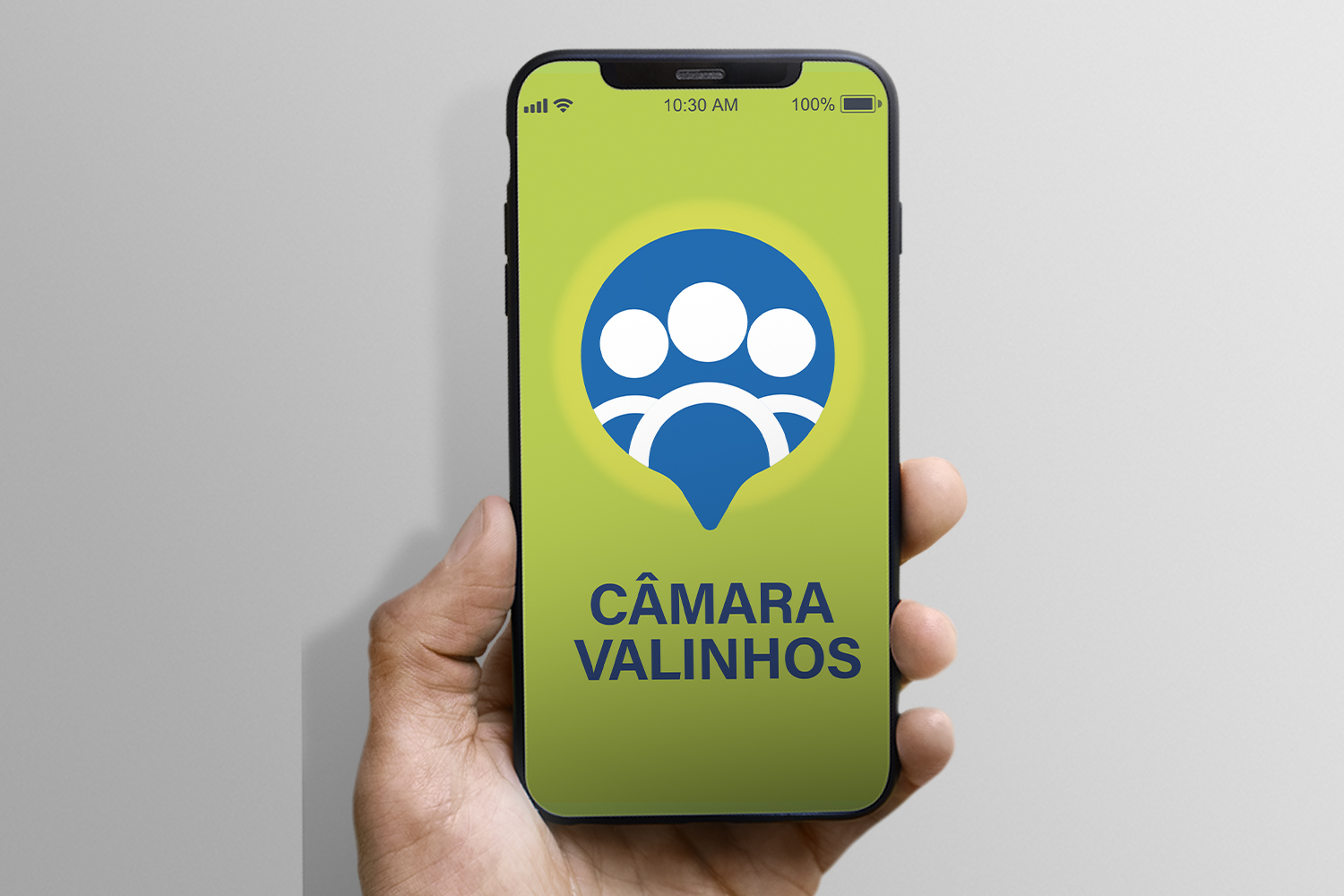 #PraCegoVer: Foto mostra mão segurando um celular. Na tela está o logotipo do aplicativo da Câmara, em que predominam as cores verde claro e azul.